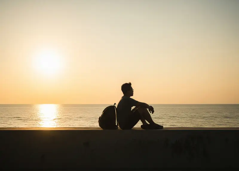 Filipino backpacker with a small bag watching the sunset by the seawall.