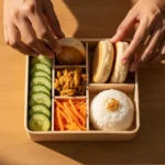 A colorful and healthy bento-style baon for a school kid, featuring rice, chicken, vegetables, and fruit in a lunchbox.