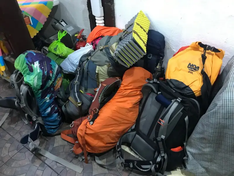 A pile of colorful hiking backpacks and gear stacked indoors, ready for a trip.