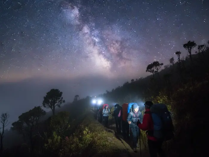 Filipino hikers trekking with headlamps during an overnight climb to Mount Pulag summit.