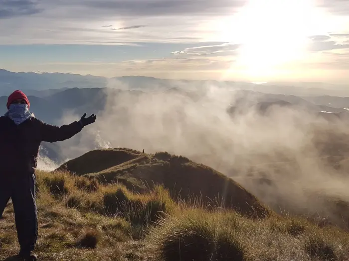 Filipino hiker raising arms at Mount Pulag summit above the rolling sea of clouds.