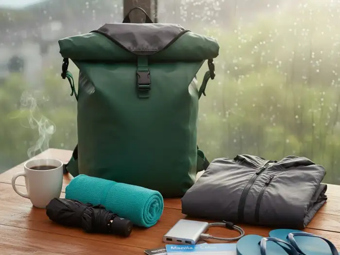 Rainy season travel essentials laid out including rain jacket, umbrella, and backpack.