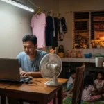 Filipino employee working a part-time online job in a modest apartment after his day job.